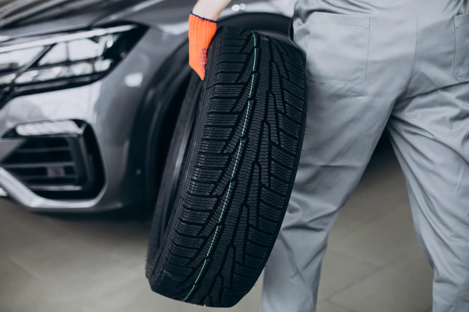 Mechanic carrying a new tyre past a car in the workshop