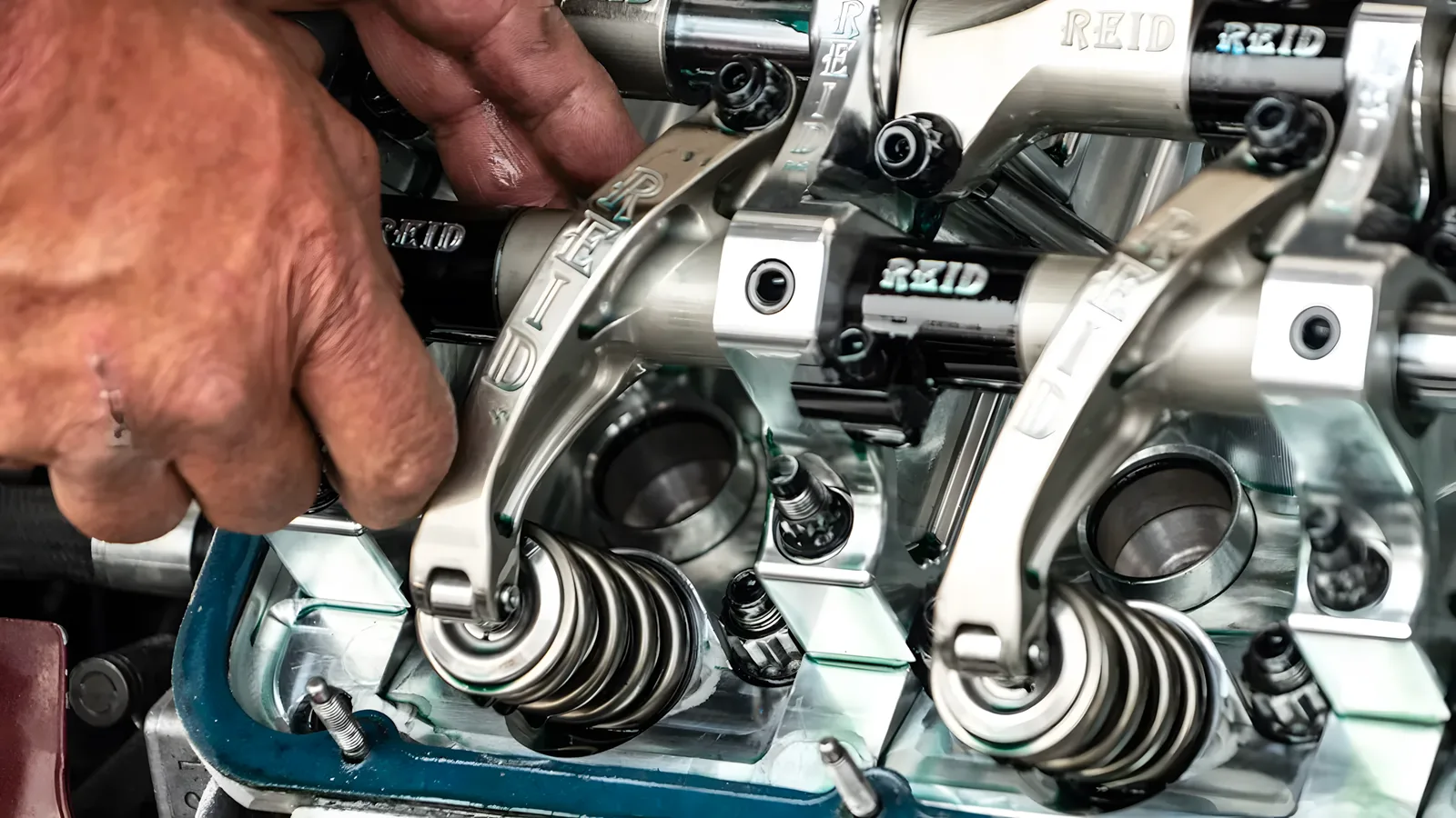 Mechanic's hand adjusting a polished rocker arm over valve springs on an exposed engine cylinder head
