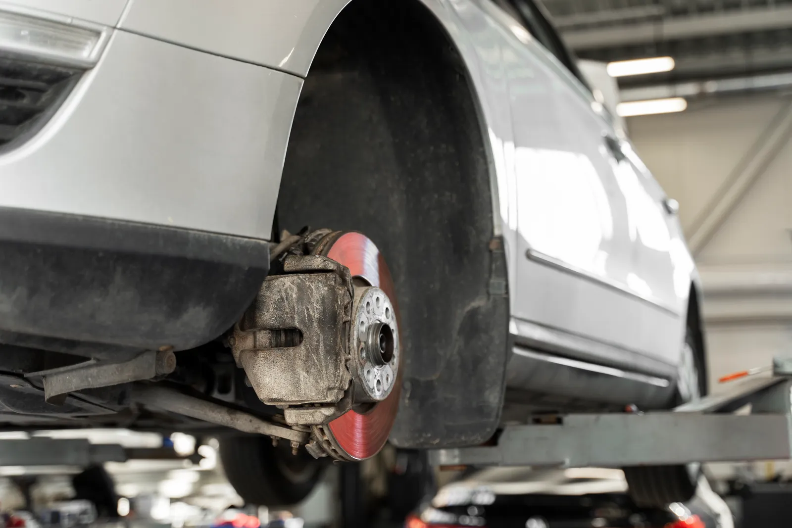 Car raised on a workshop hoist with a front wheel removed, showing the brake disc and caliper