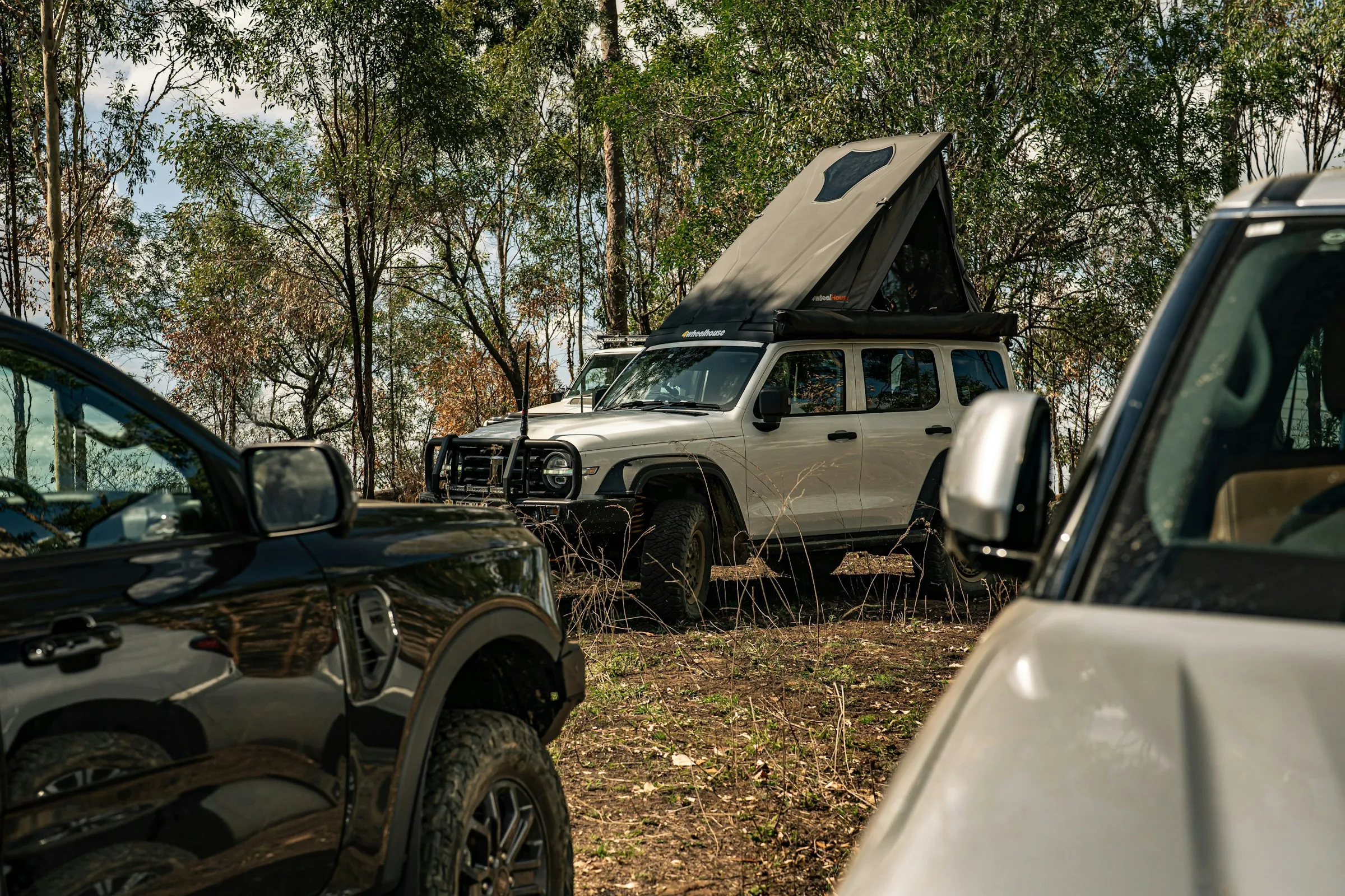 White 4WD with a rooftop tent set up at a bush campsite among gum trees